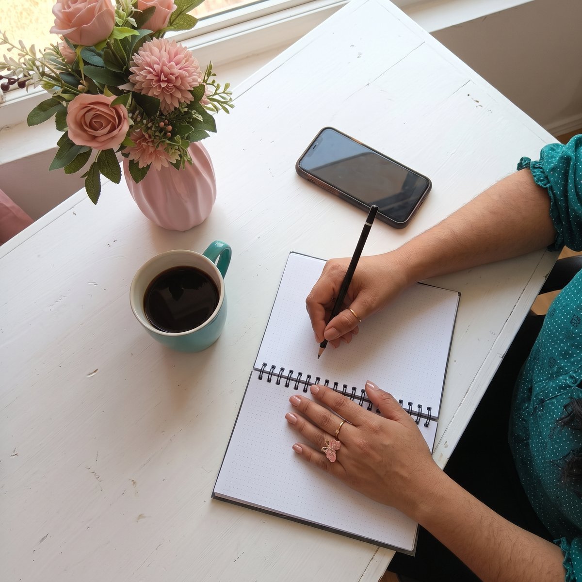 Manos de Erentira escribiendo en una libreta junto a una taza de café